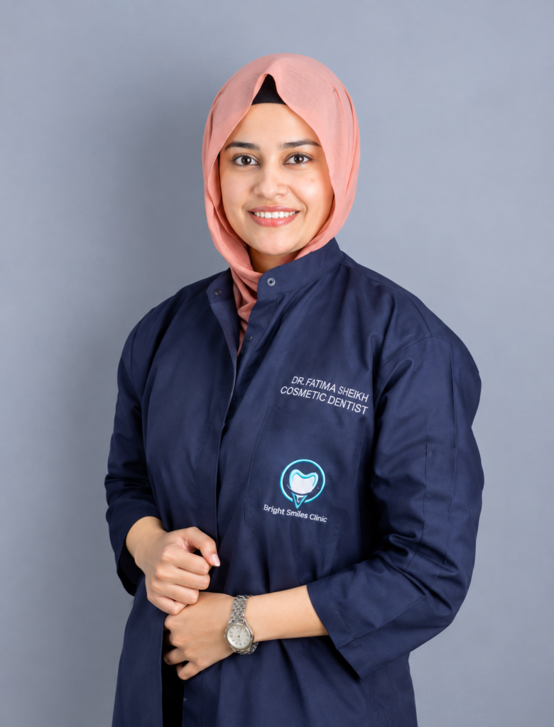 Smiling dentist in a navy coat with "Dr. Fatima Sheikh, Cosmetic Dentist" embroidered, representing Bright Smiles Clinic.