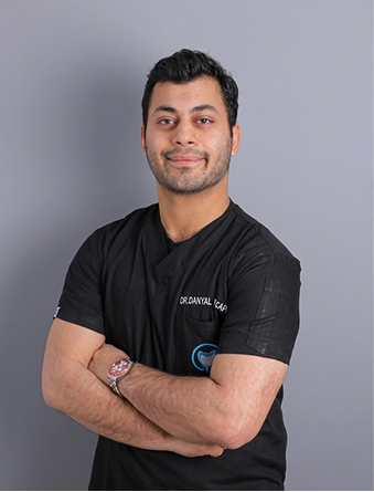 Smiling man in black scrubs with folded arms against a gray background.