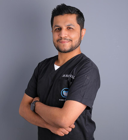 Smiling man in black scrubs with folded arms against a gray background.