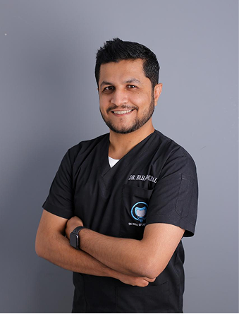 Smiling man in black medical scrubs with arms crossed against a gray background.